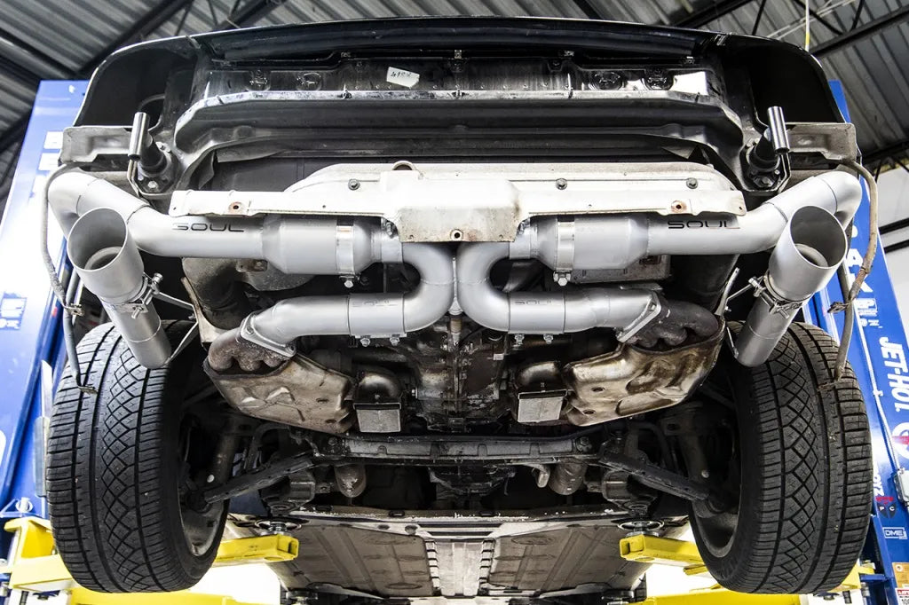Underside of engine with Soul Performance sport muffler bypass exhaust system in silver installed on Porsche 993 on a garage lift.