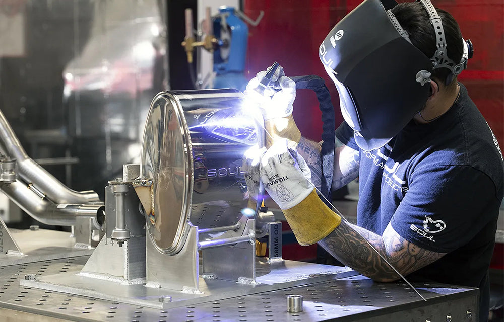 Person welding Soul performance sport side muffler for Porsche on a work table.