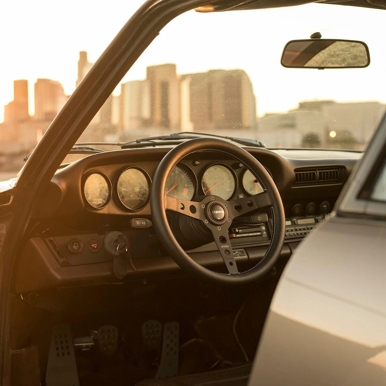 Momo Prototipo steering wheel installed on a Porsche 911 SC classic interior with downtown skyline in background.