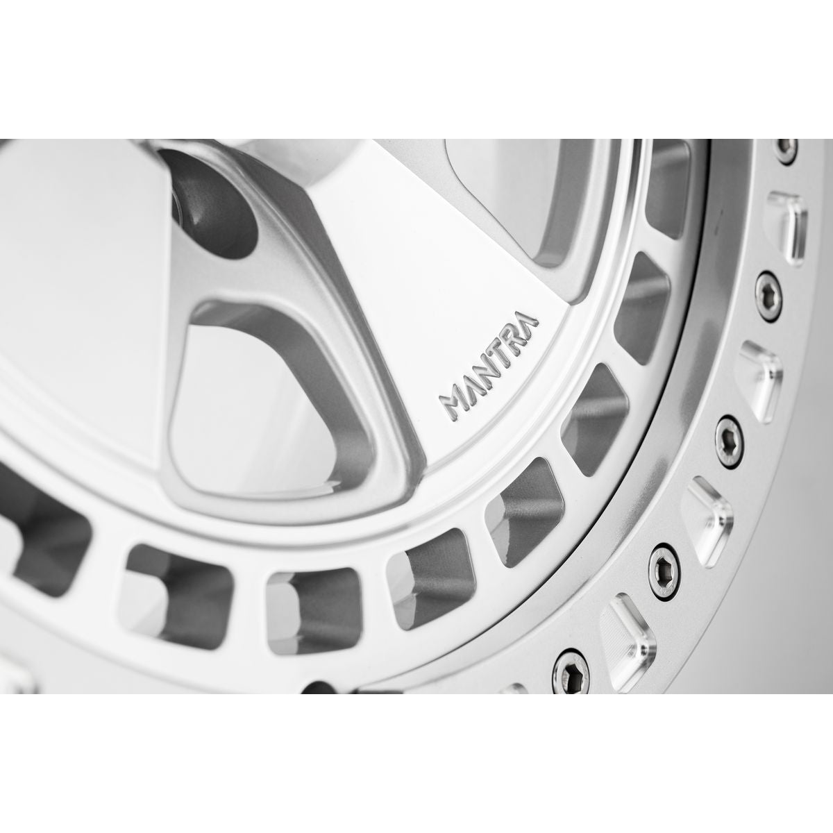 Close up of beadlock and 'MANTRA' logo on silver forged alloy off-road wheel for Porsche Cayenne on a white background.