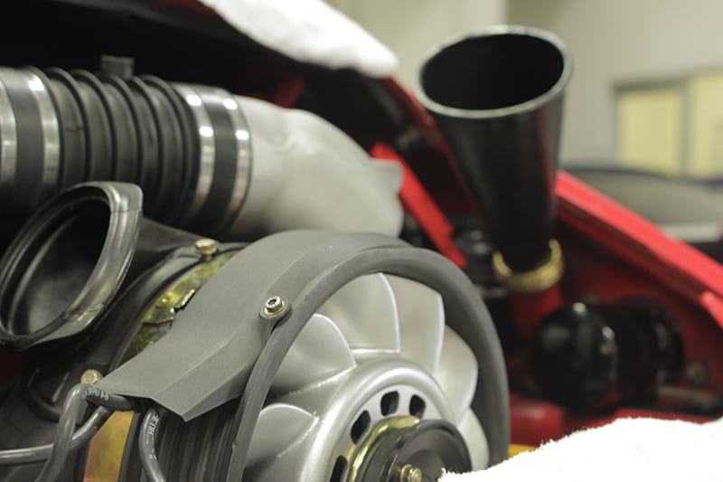 Close-up of a Porsche 911 air-cooled engine with visible fan and oil funnel.
