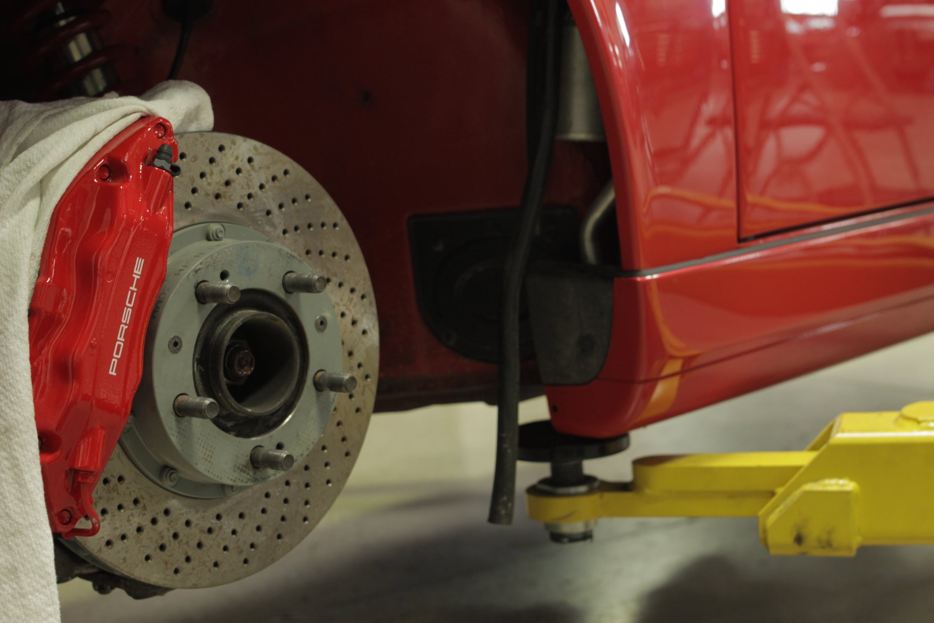 Close-up of a red Porsche 911 front brake system on a yellow garage lift.