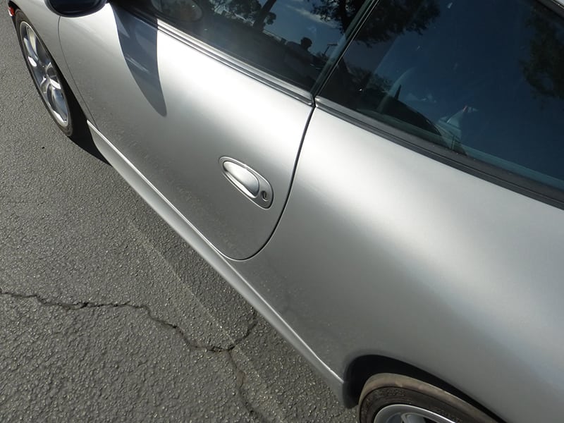 Close-up of a Porsche 996 911 silver door on asphalt.