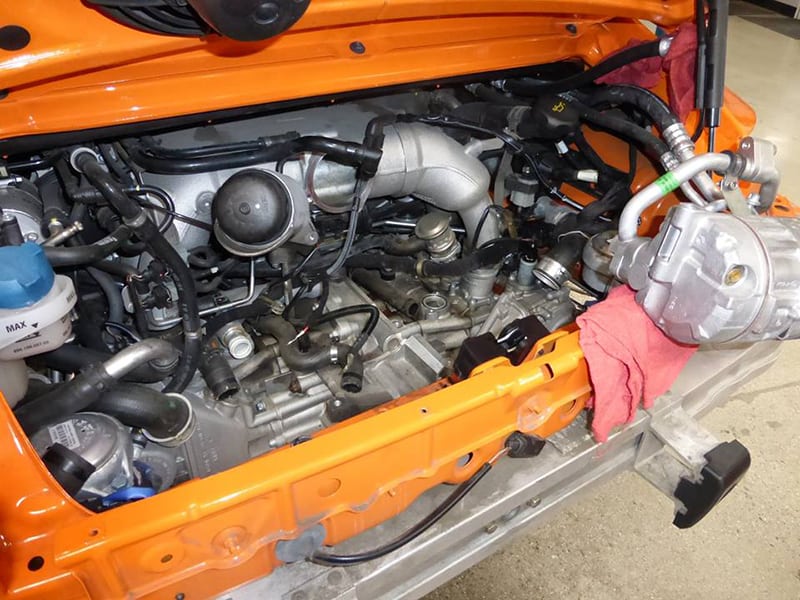 Engine compartment of an orange Porsche 911 with visible components.
