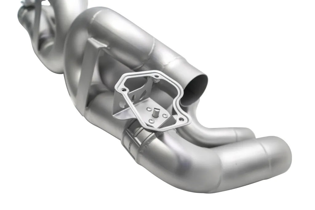 Close up of Soul Performance center muffler bypass X-pipe valved exhaust system in silver for Porsche 911 on a white background.