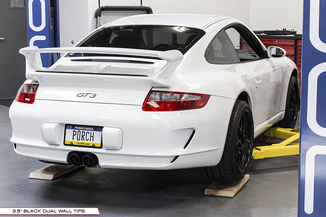 Soul Performance center muffler bypass exhaust system with black exhaust tips installed on white Porsche 997 911 GT3 on garage lift.