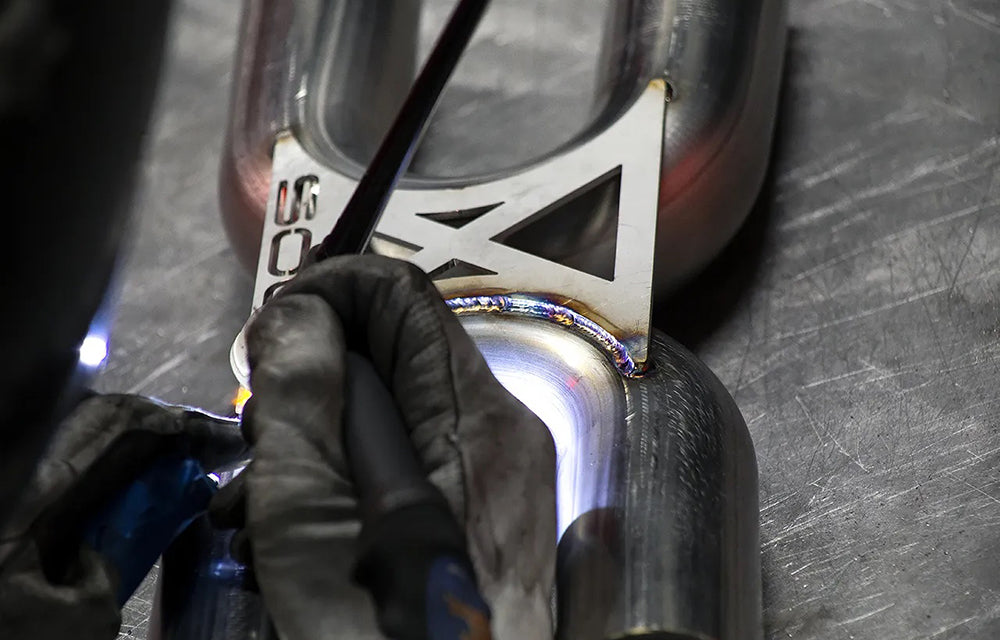 Person wearing gloves welding a Soul Performance exhaust pipe with a brand logo.