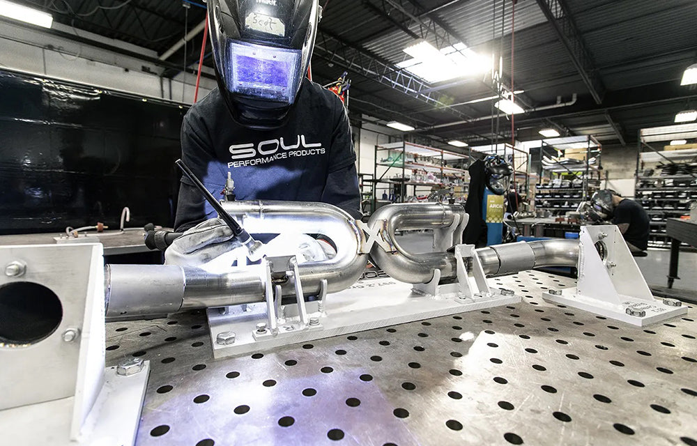 Person welding Soul Performance center muffler bypass pipes in a workshop with 'Soul Performance Products' branding on shirt.