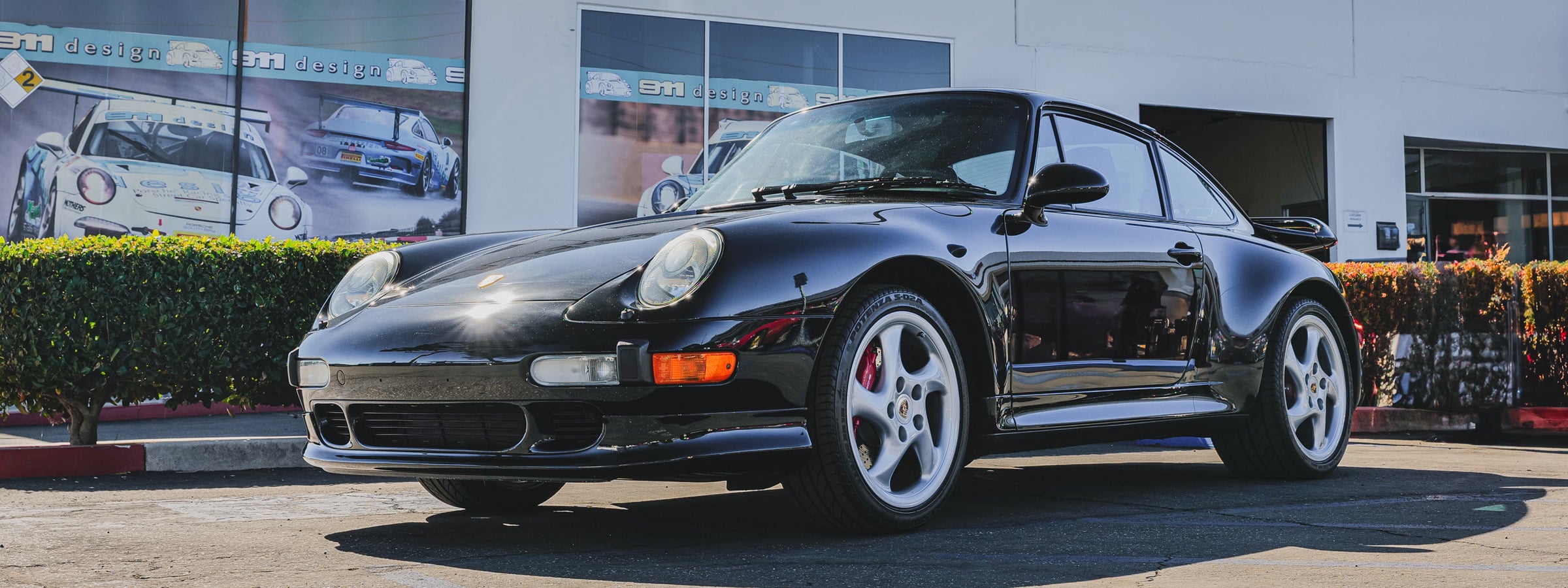 Black Porsche 911 993 parked in front of a 911 design building.