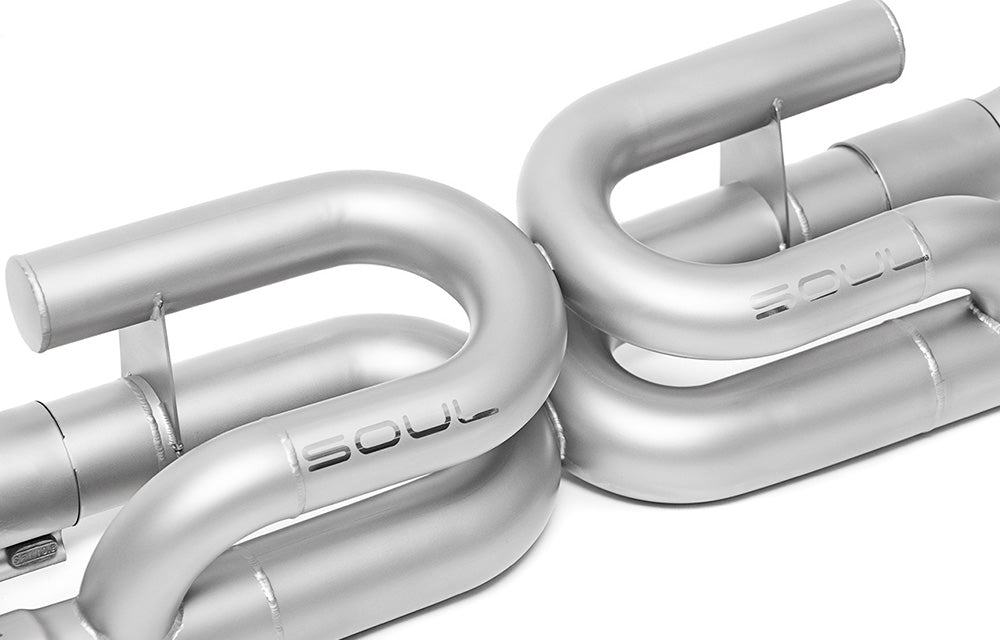 Detail of welding and piping on a Soul Performance exhaust with anti-drone tube for Porsche 991.2 Carrera base, finished in silver on white background.