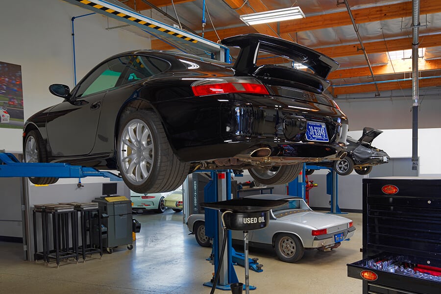 Black Porsche 996 911 GT3 on a lift in a garage with various tools and equipment.