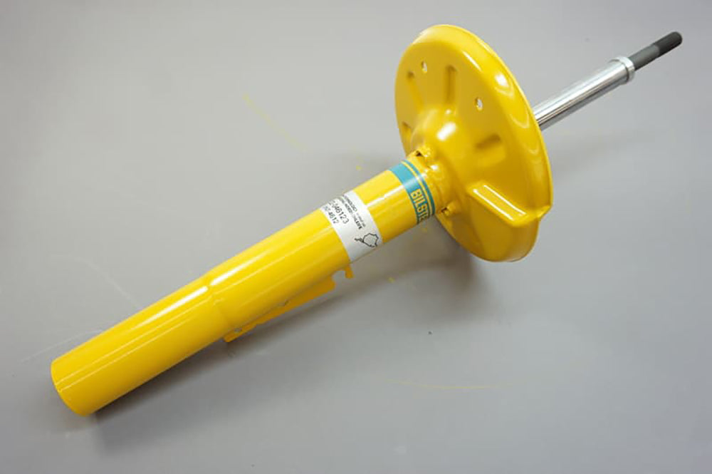 Yellow Bilstein shock absorber for Porsche on gray background.