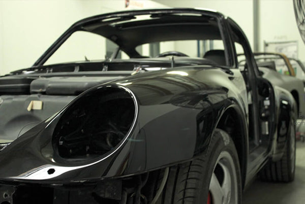 Front 3/4 view of black Porsche 911 in body shop.