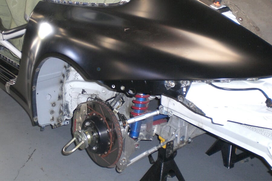 Close-up of a black Porsche 911 rear suspension and brake system with visible components on jack stands.